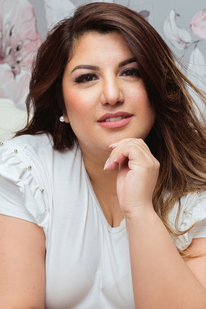 Primer plano de Daiana, CEO de DR Estética, con una expresión cálida y profesional. Lleva una blusa blanca con detalles decorativos y un fondo floral suave que complementa su imagen inspiradora.